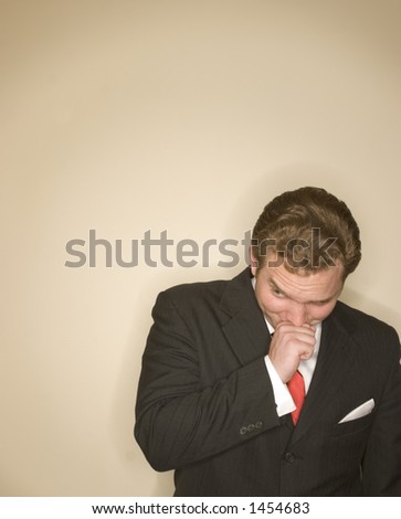 Business man in black suit, white shirt, and red tie against a tan background is holding his hand up to his face in a clever expression