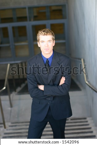 Blond hair blue eye business man is wearing a dark blue suit with a blue shirt and a black tie as he is looking directly at you