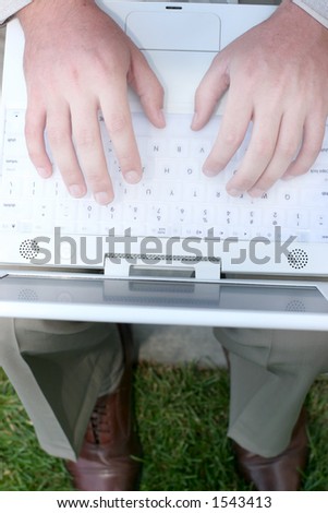 Businessman has hands on top of white laptop as he sits on a bench in the green grass