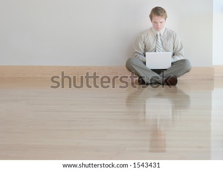 Businessman in tan shirt and tie is typing on his white laptop on wooden floors