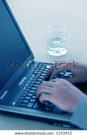 Businessman types on laptop with glass of water on the table