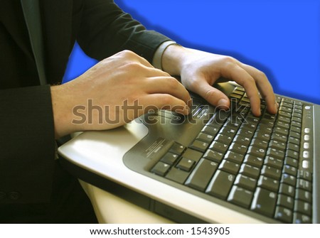 Businessman black suit and dark green shirt is busily typing on his laptop keyboard against a blue backdrop