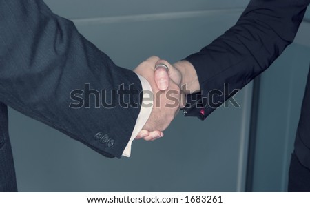 Business man and woman shake in front of a glass background