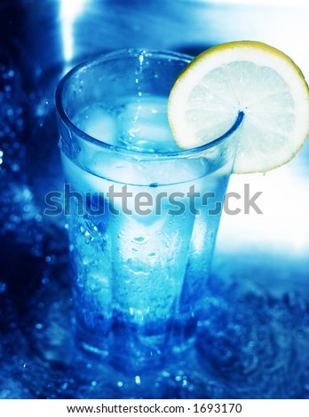 Glass of cool water has lemon slice around its edge as it is surrounded by rushing water