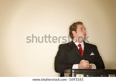 Business man in black suit is folding arms on top of his briefcase