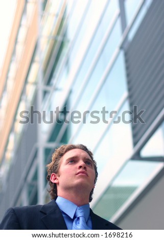 Busines man in dark suit, blue shirt, and blue tie poses in front of office building