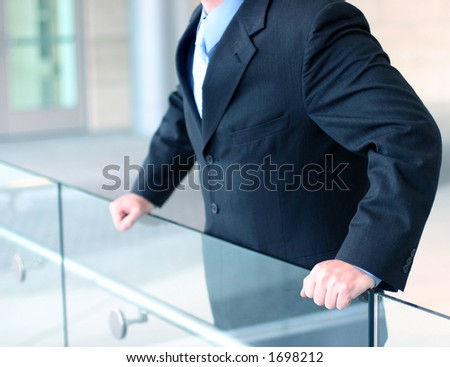 Business man in darker suit, blue shirt, and blue tie holds the edge of a glass wall