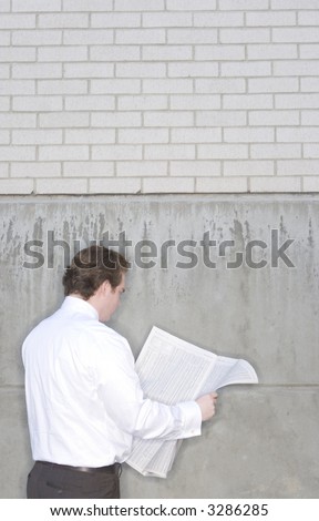 Businessman standing outside reading a newspaper in front of a brick building