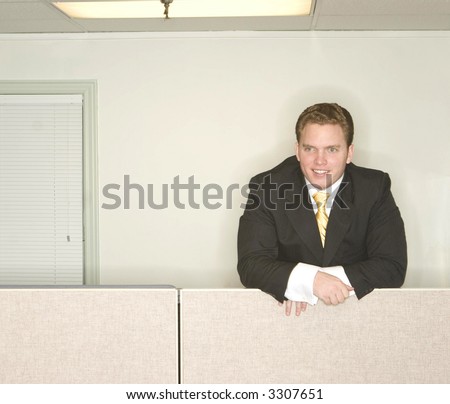 Businessman stands and looks ahead with a smile on his face while standing above his office cubicle