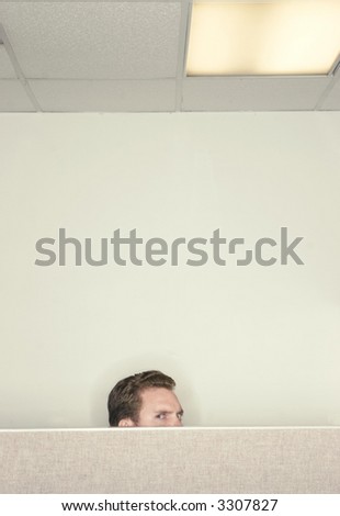 Businessman looking back over the cubical wall with a suspicious look on his face