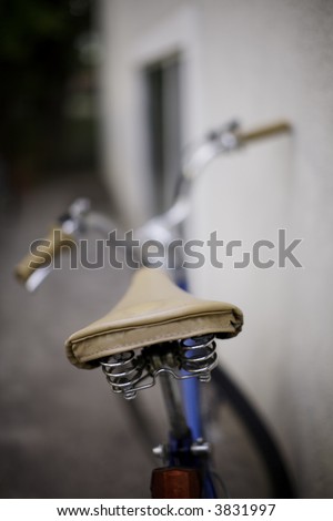 a bicycle sits against the wall in the summer time with the focus on the seat in the foreground