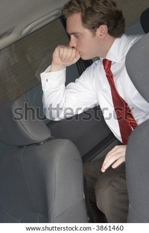 Businessman sitting in the back of the car contemplating while he wears a red tie and a white business shirt