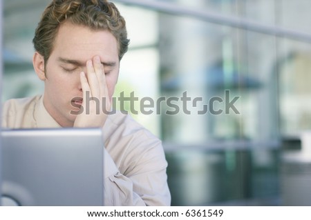 One young business man with head in hands with laptop in front