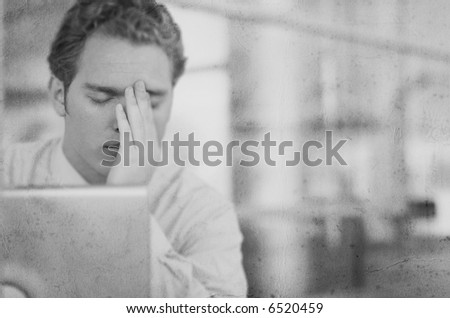 Black and White of one young business man with head in hands with laptop in front