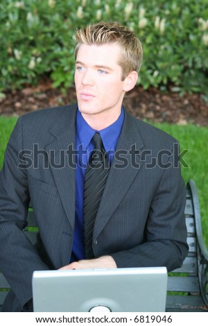 close-up waist-up view of young blue blond hair businessman sitting on bench holding laptop looking away