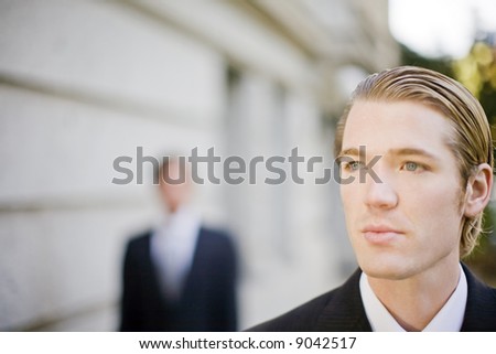 two businessmen standing in front of building wearing suits looking past camera