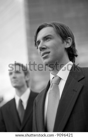 two businessmen standing side by side looking forward in front of tall blue office building