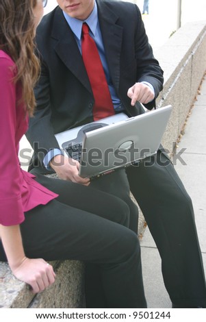 businessman and businesswoman sit outside face each other with laptop between them
