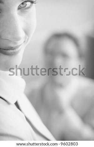 Beautiful businesswoman and man look off in same direction with woman's face up close and man's face blurred in the background