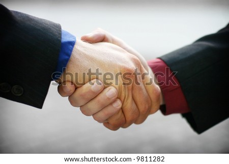 Firm business handshake with red and blue shirts and black suits against gray background