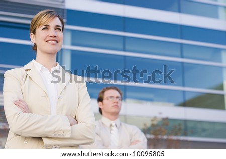businesswoman and businessman standing side by side with arms folded looking forward