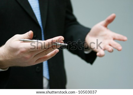 close up of hands gesturing while holding pen and torso of man with business suit and blue tie