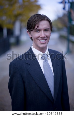 front view of single white young businessman standing looking at camera with office buildings in background
