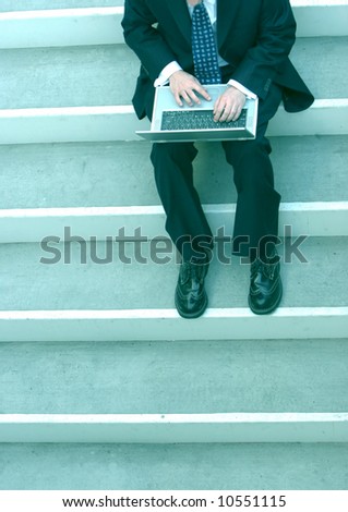 Over-head view of young businessman sitting on stairs typing on laptop