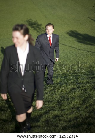 Two businesspeople climbing hill together wearing full suits and smiling