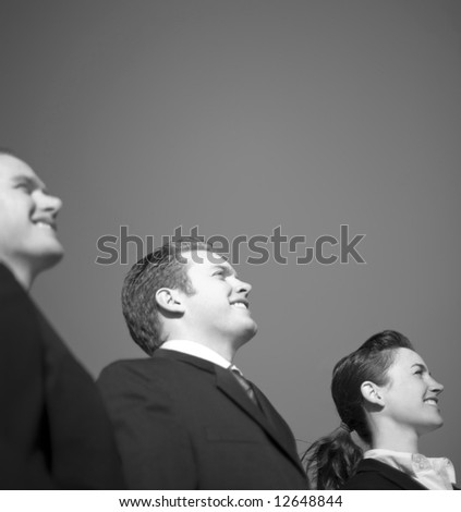 Three business people in suits standing in a row smiling and looking in the same direction with a blue sky background