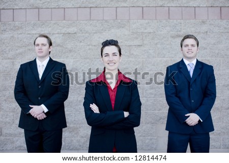 Three attractive business people in suits stand next to each other all facing forward
