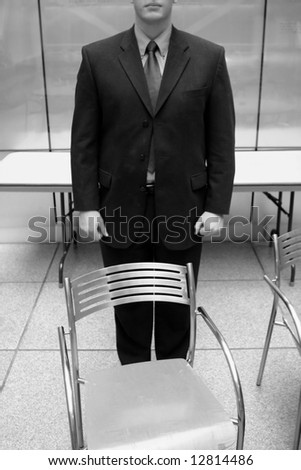 Businessman dressed in full suit standing behind empty office chair