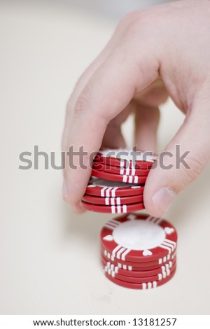 man holding red gambling chips in his hands is counting them as he waits for his gambling bet to come