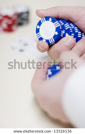man holding gambling chips in his hands that are blue waiting to make a bet while gambling with a deck of cards