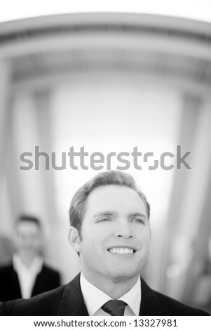 front view of young businessman standing wearing suit with businesswoman standing behind him
