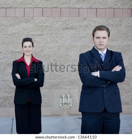 businessman and businesswoman in formal wear standing with arms crossed