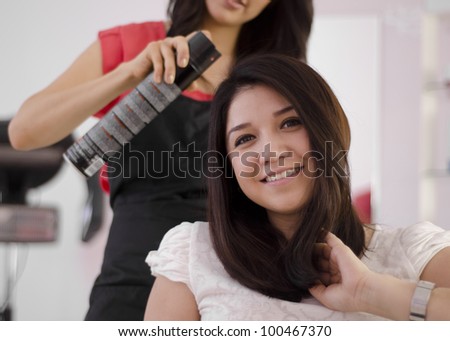Young female hairdresser applying spray on client\'s hair
