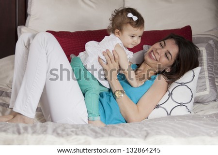 Cute latin mother and baby girl having some fun in the bedroom