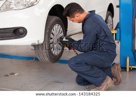 Hispanic young mechanic using an air gun to tighten the bolts of a tire from a suspended car