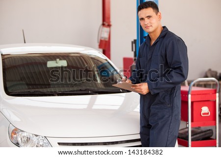 Handsome young man holding a checklist in front of a car in an auto shop