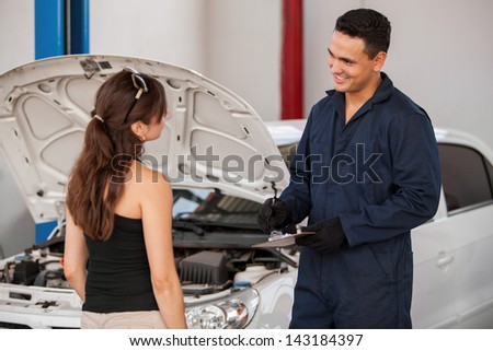 Handsome young mechanic receiving a car at an auto shop from a female customer and smiling