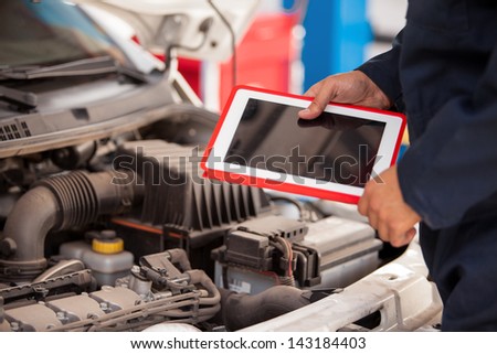 Closeup of a mechanic using a tablet computer next to an open hood in an auto shop