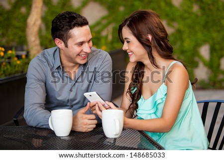 Happy young couple looking at something on a cell phone while having coffee at a restaurant