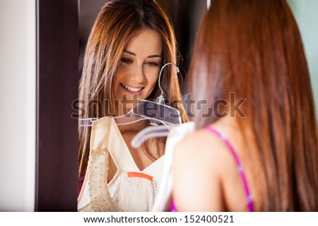 Pretty Latin woman trying on a new dress in front of a mirror and smiling