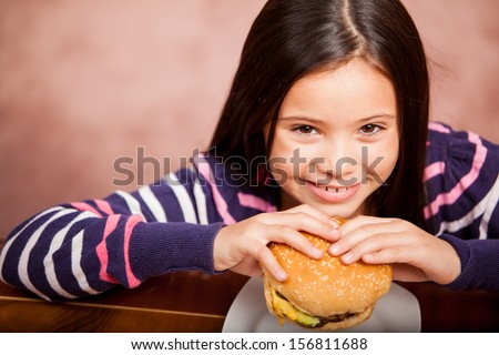 Portrait of a happy little girl eating a hamburger, shot from a high angle