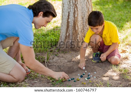 Cute young boy playing with marbles outdoor with his father