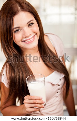 Happy young woman drinking milk from a glass at home