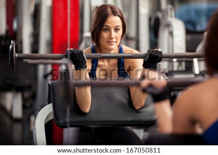Pretty young woman lifting a barbell in front of a mirror at the gym