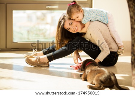 Beautiful young Hispanic mother with a baby girl and a cute Labrador puppy at home