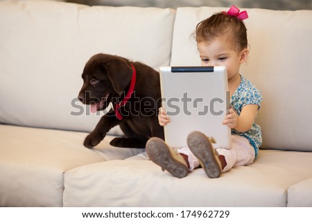Cute little girl watching a movie on her tablet computer while her dog keeps her company